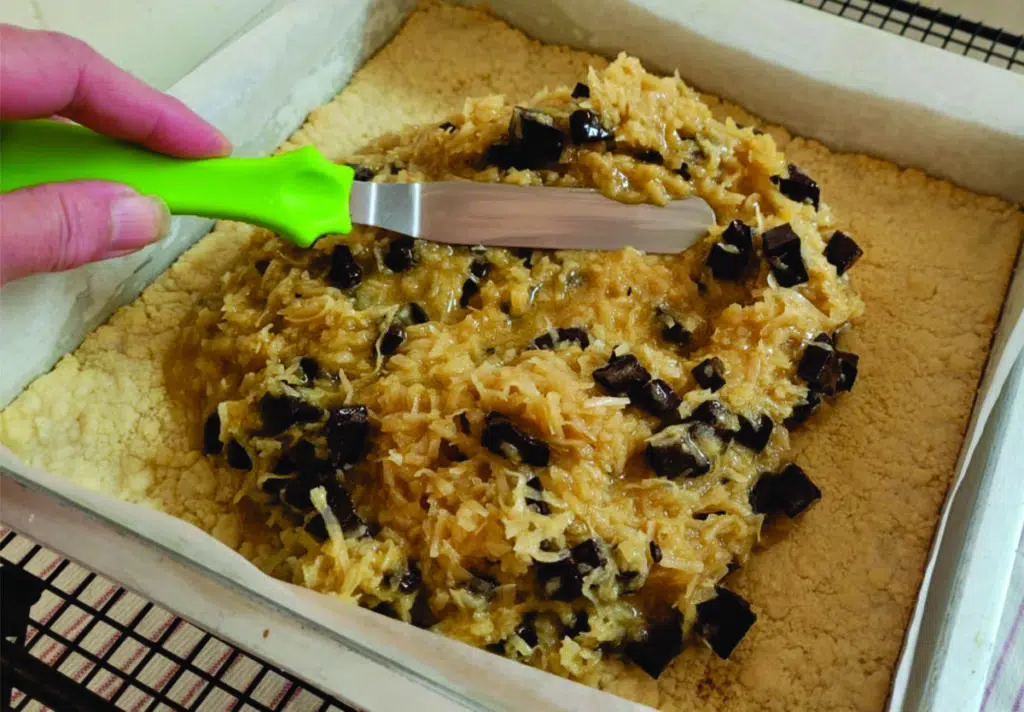 spreading coconut in pan for dessert bars