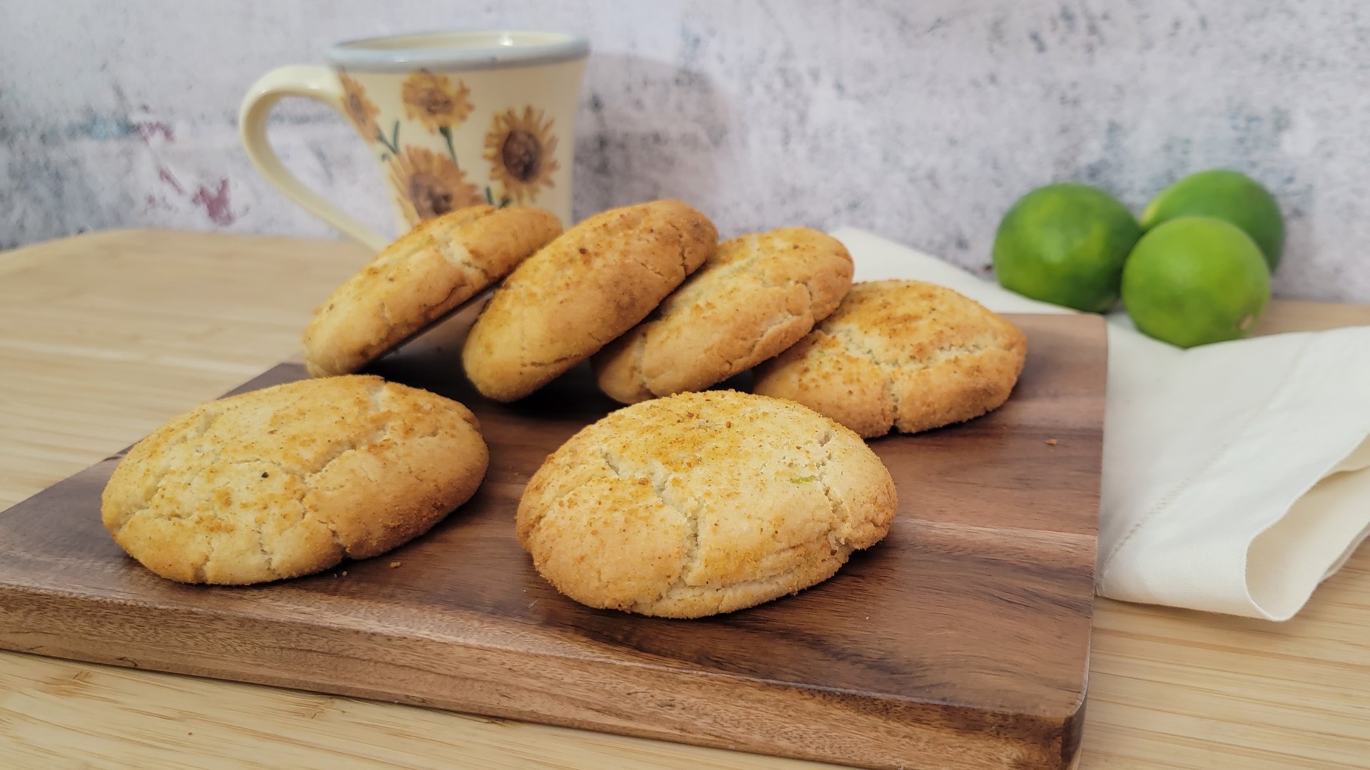 key lime pie cookies on a wooden board with a coffee cup and limes in the background