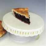 slice of blueberry pie on a serving platter with full pie in background