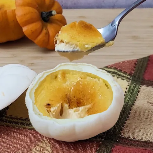 spoon with pumpkin crème brulee baked in a mini pumpkin