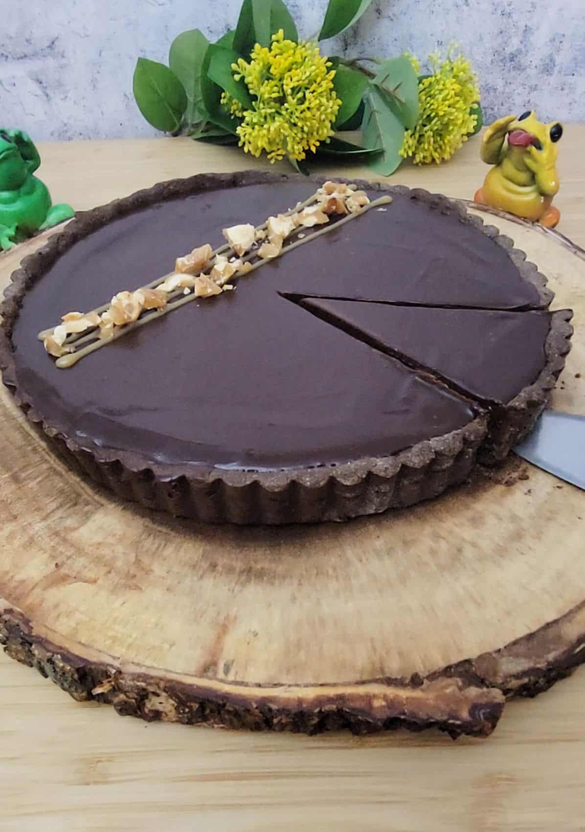 PB caramel tart covered in chocolate and sitting on a wooden tray