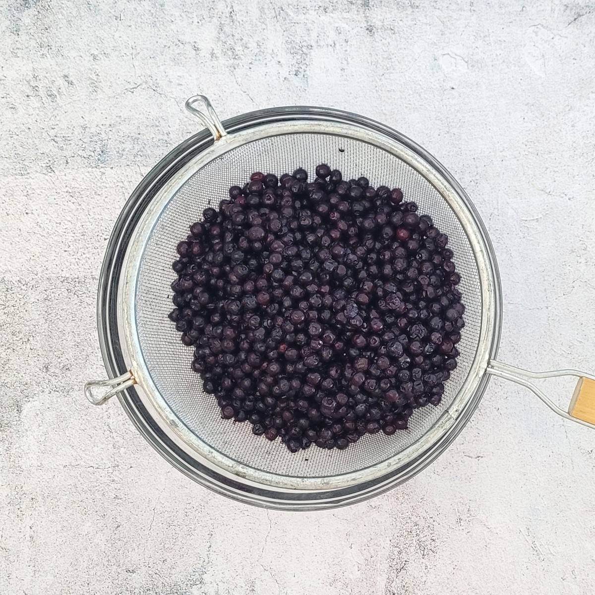 frozen blueberries in a sieve being drained to reserve juice