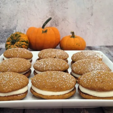pumpkin whoopie pies on a white platter with pumpkins in background