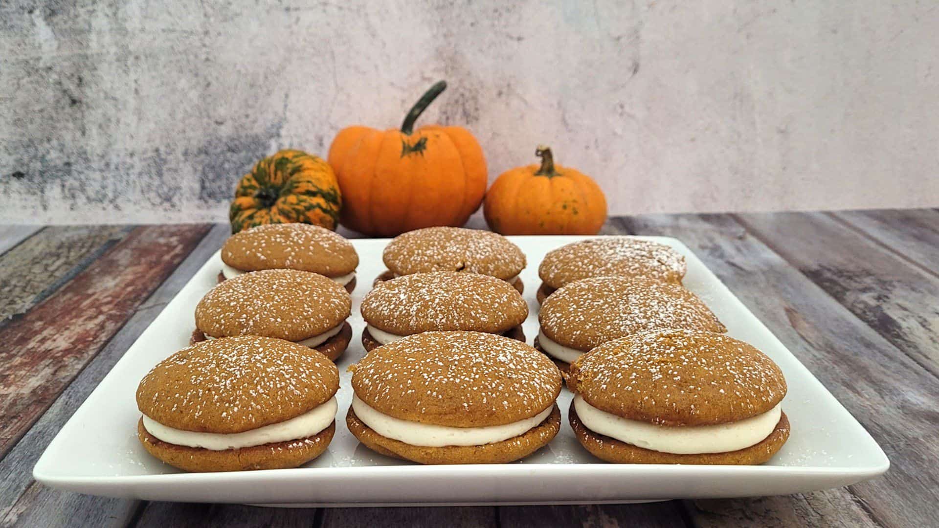 pumpkin whoopie pies on a white platter with pumpkins in background