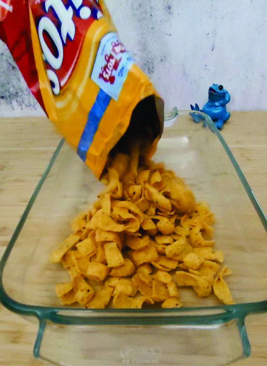 pouring a bag of Fritos into a glass baking pan