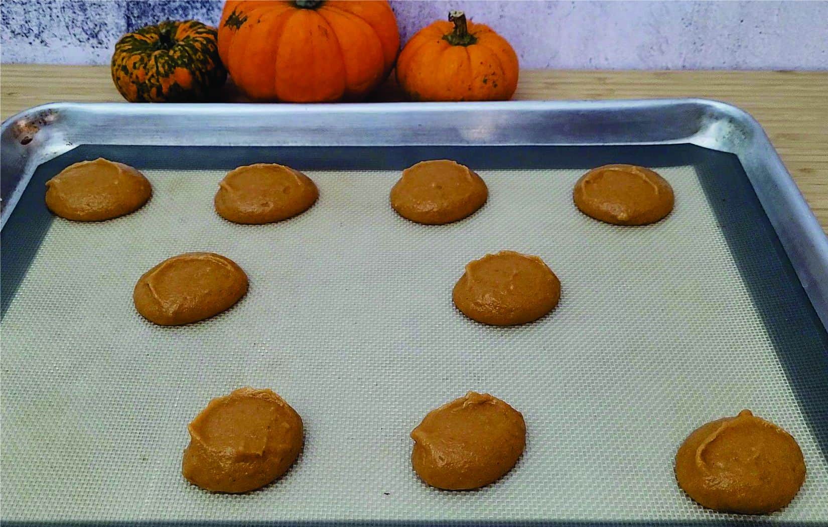 scooping pumpkin whoopie pies onto a sheet pan lined with a silicone baking mat