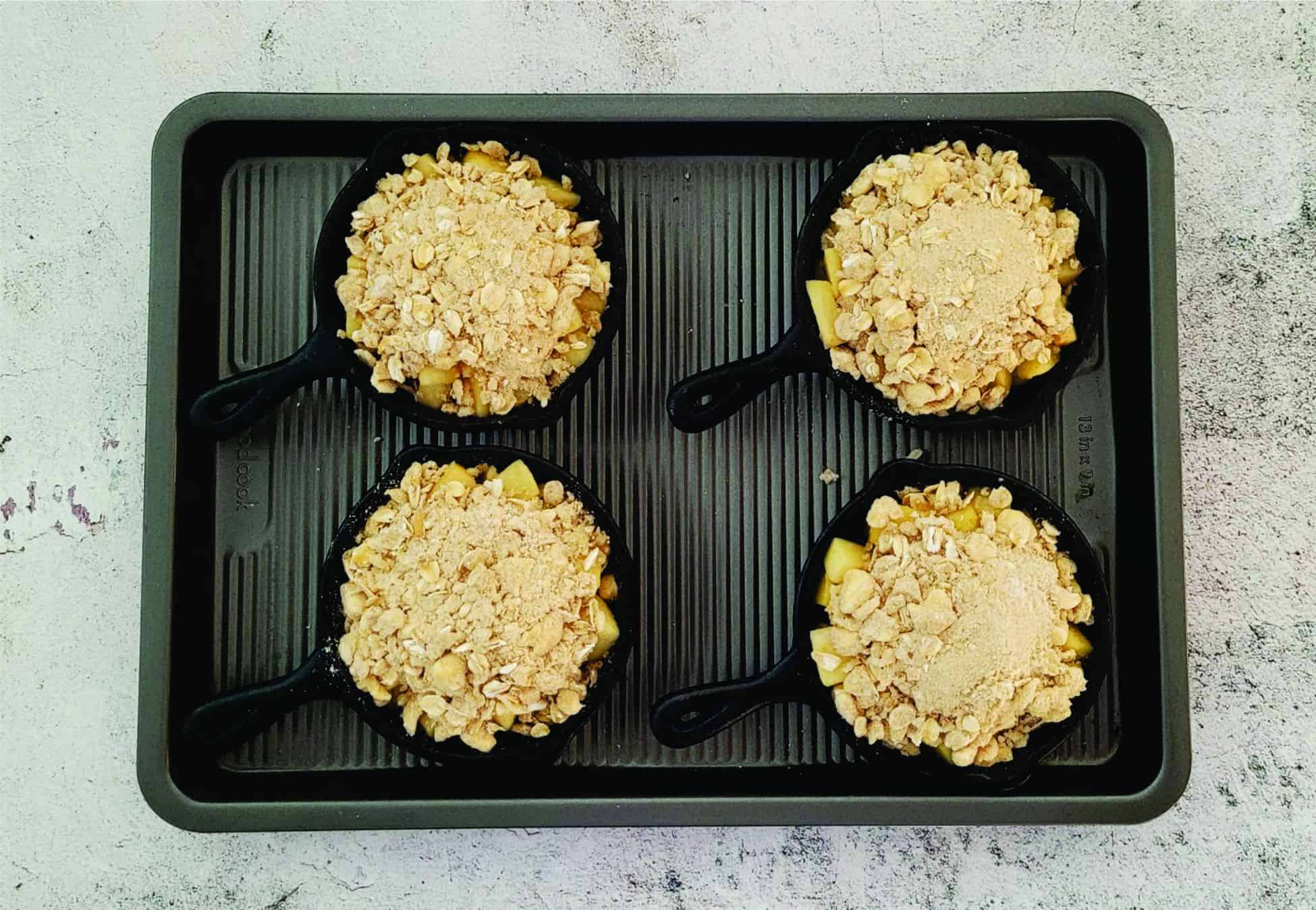filled mini cast iron skillets with apple filling and crisp topping ready for baking