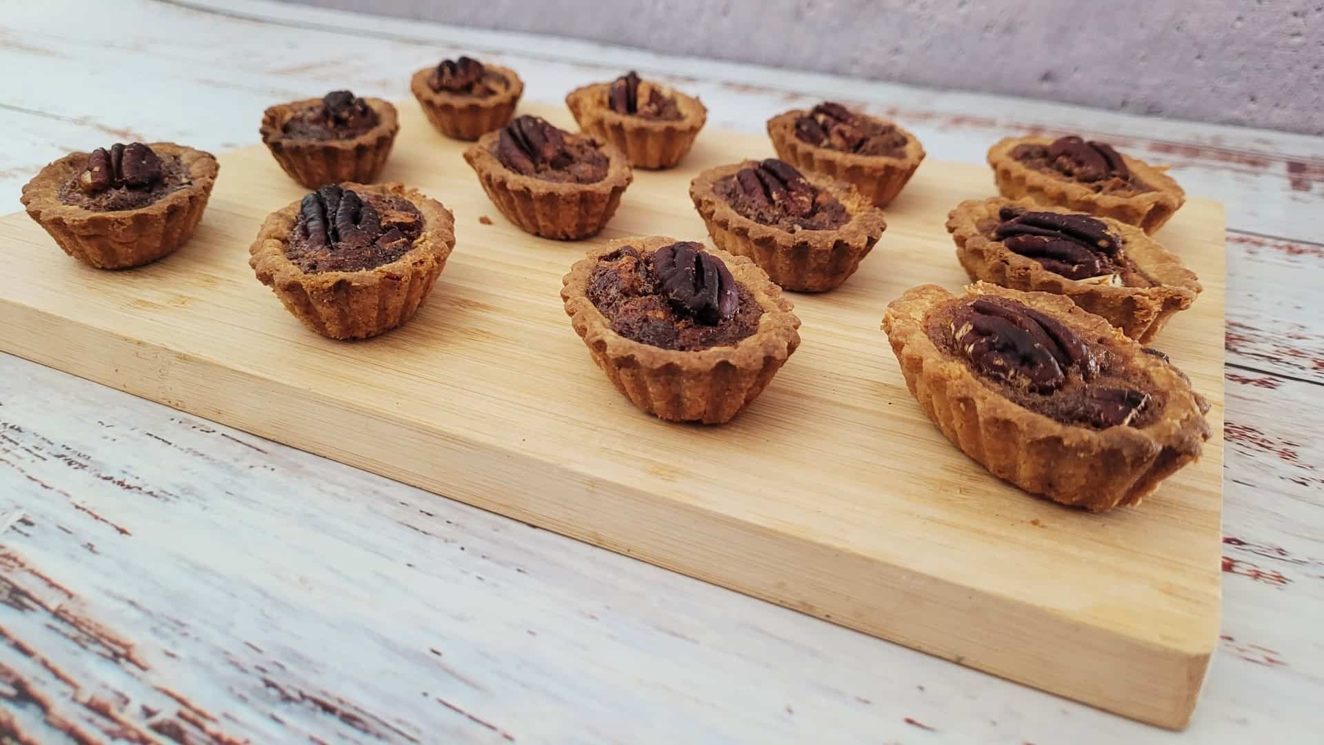 12 mini pecan pies baked and set on a wooden serving platter