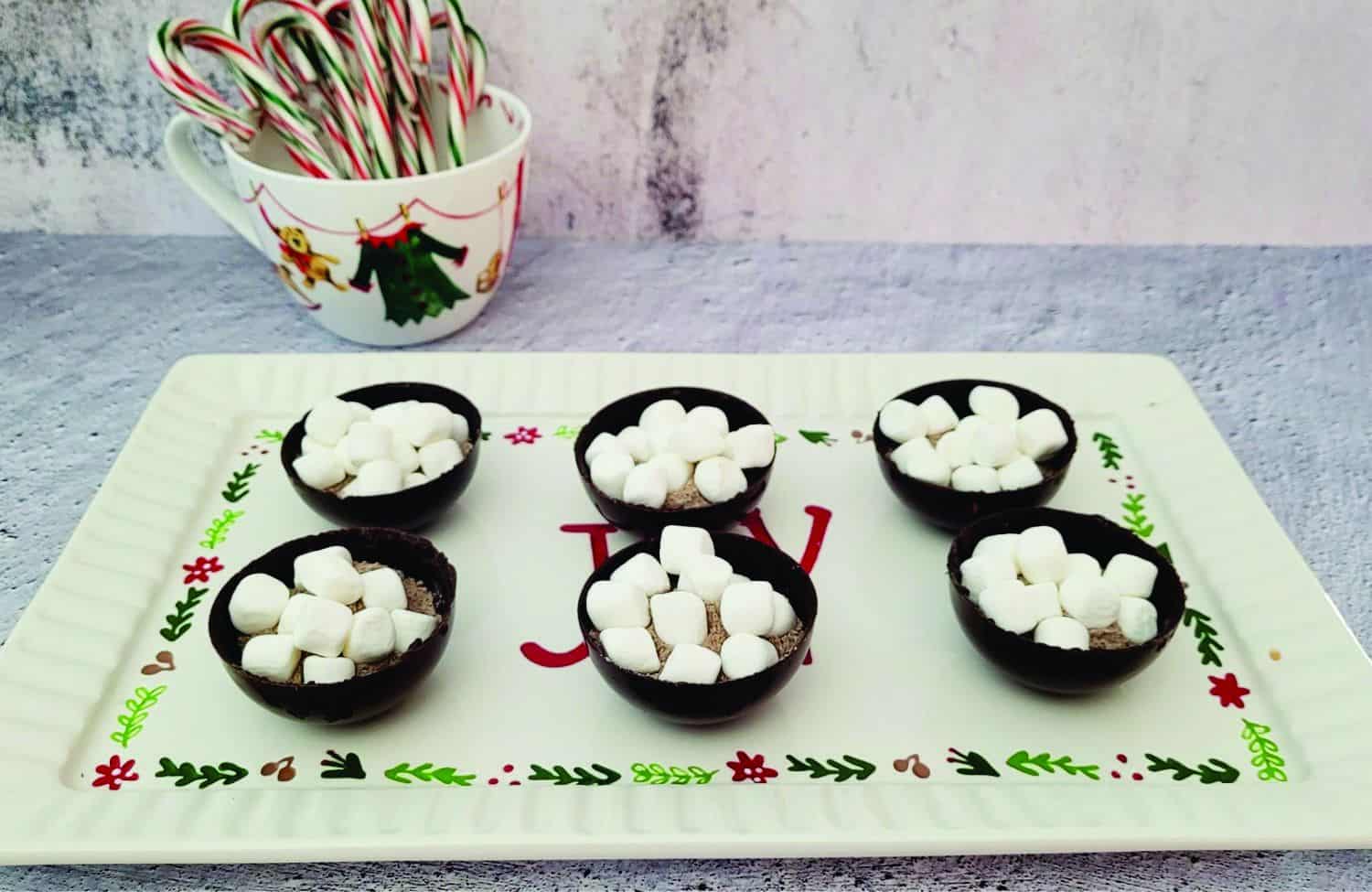 six chocolate spheres filled with hot cocoa mix and marshmallow sitting on a Christmas platter