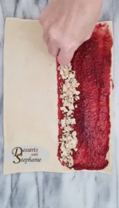 sliced almonds being sprinkled over a sheet of puff pastry with raspberry jam