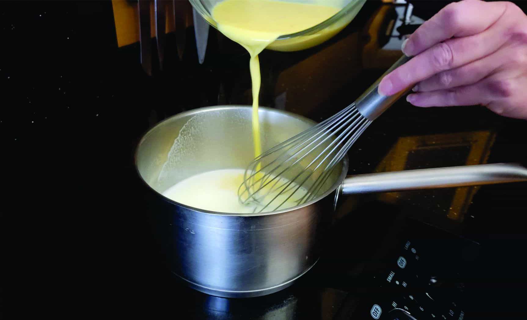 pouring eggs into milk mixture in a saucepan on stovetop