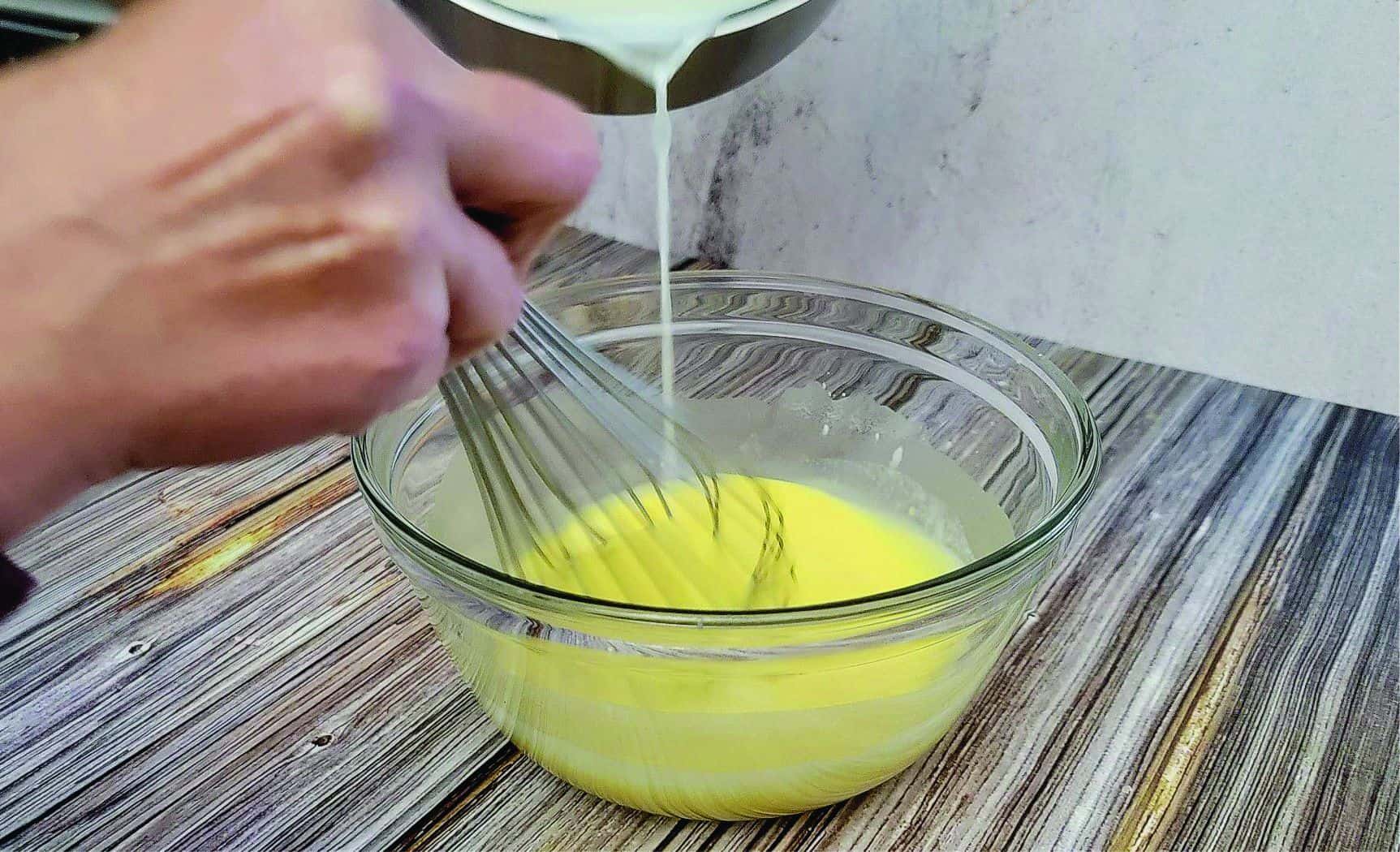 pouring hot milk into egg mixture and whisking to temper eggs