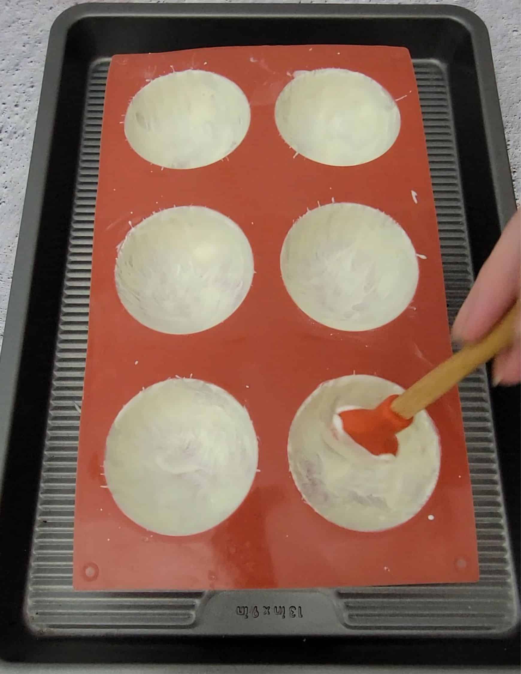 using a brush to paint second coat of white chocolate half spheres into a silicone mold