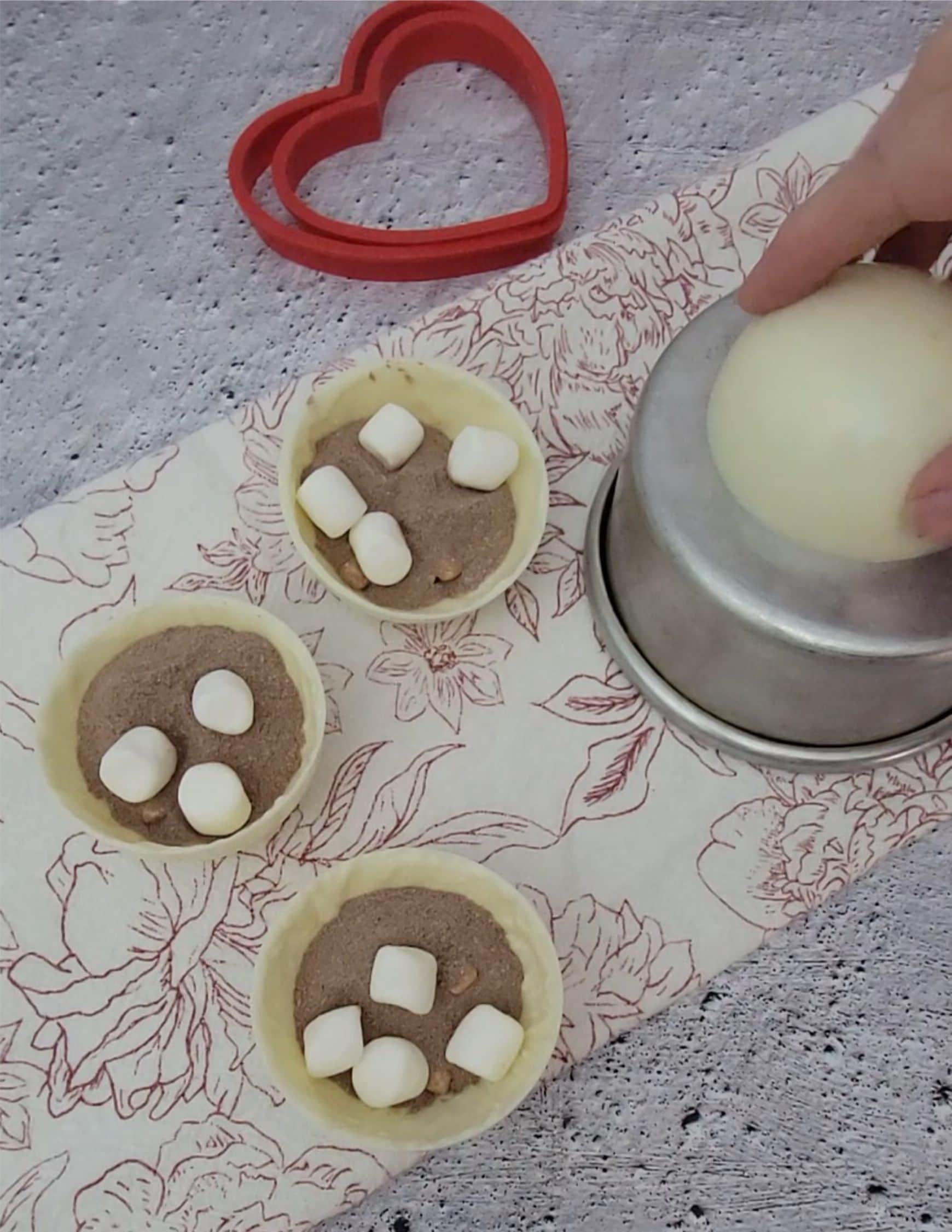 inside of hot cocoa bombs filled with mix and marshmallows and one half of chocolate sphere being heated on a cake pan