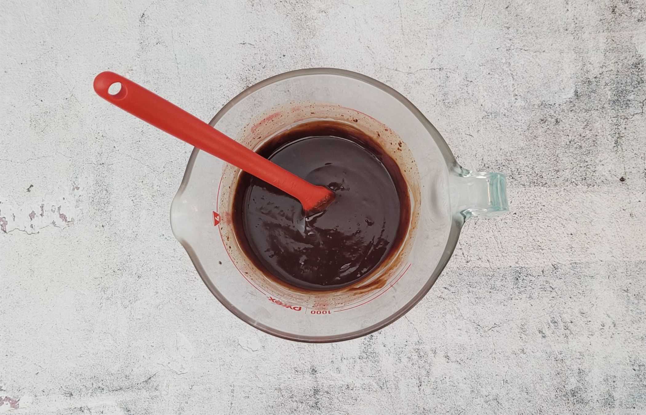 overhead view of chocolate ganache in a glass bowl being stirred with a spatula