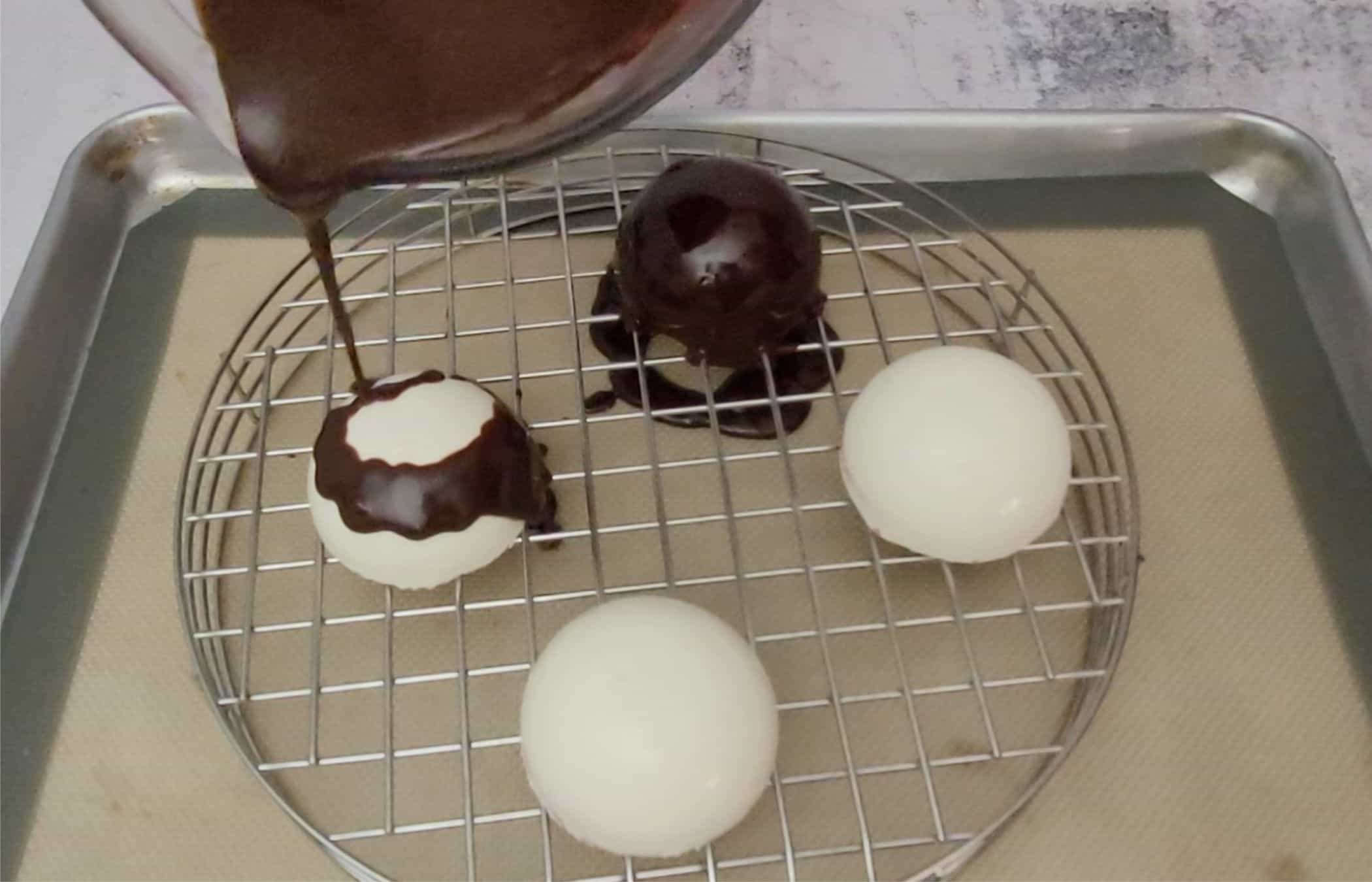 pouring chocolate ganache over four mini red velvet cakes