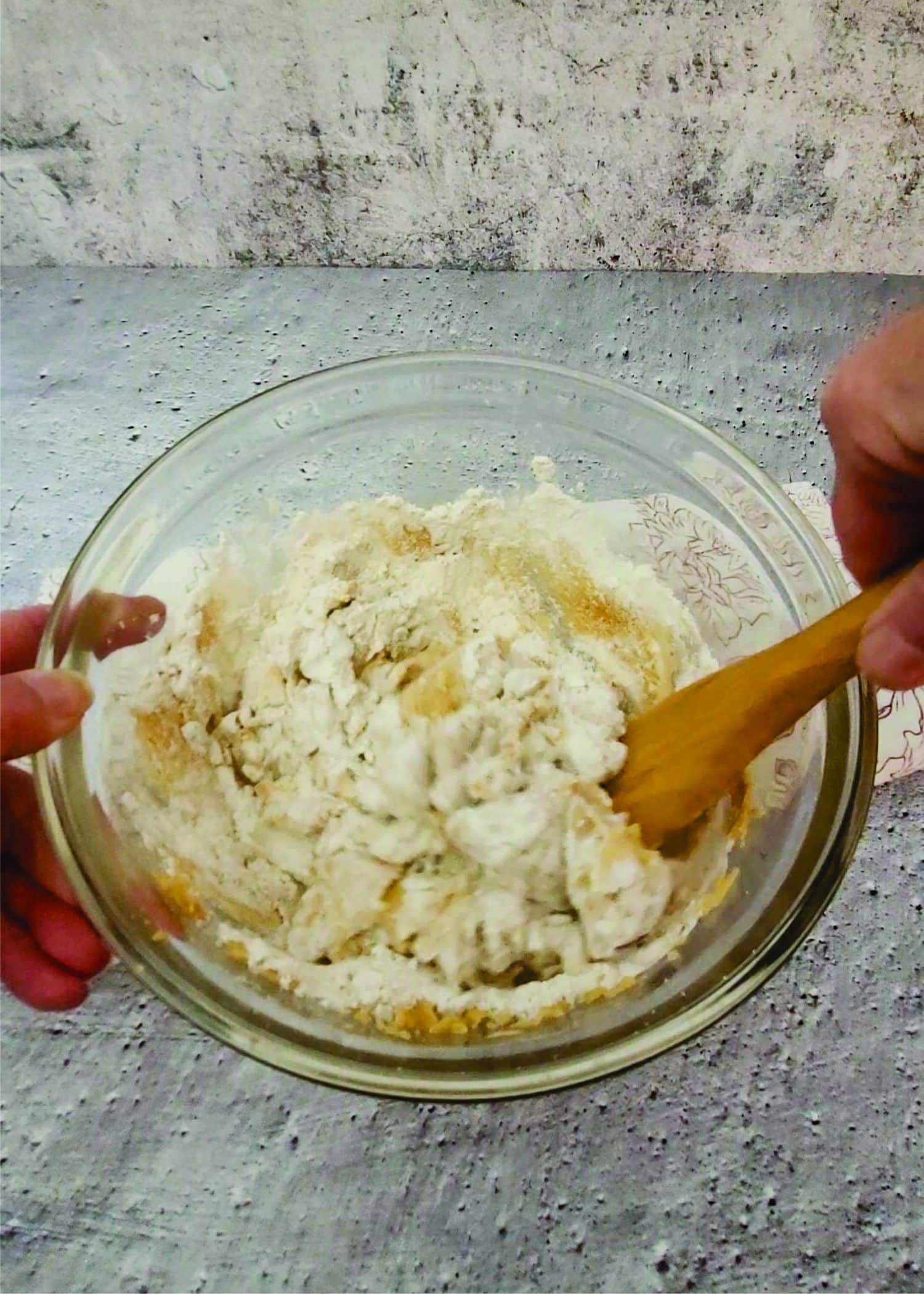 using a wooden spoon to stir flour into bowl to finish creating cookie dough