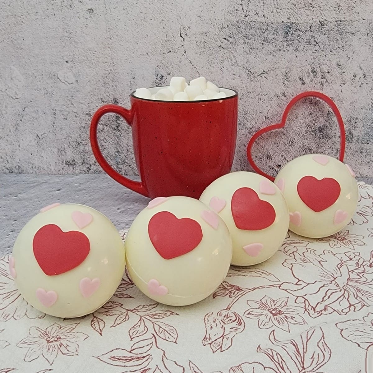 hot cocoa bombs for Valentine's day lined up in a row and one mug with hot chocolate made