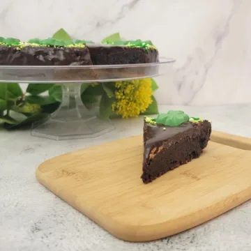 slice of St Patrick's Day flourless cake on a wooden board with the remainder of cake in the background