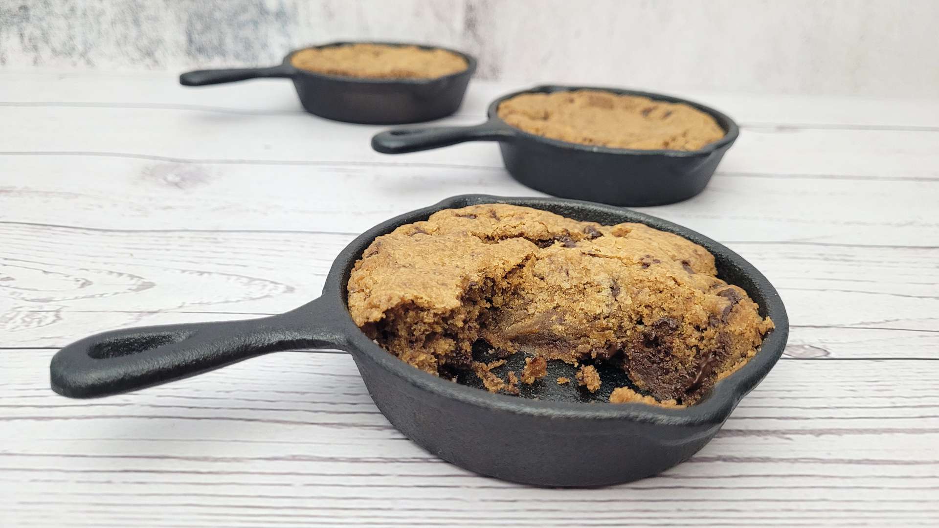 mini cast iron skillets with chocolate chip cookie and one is cut into
