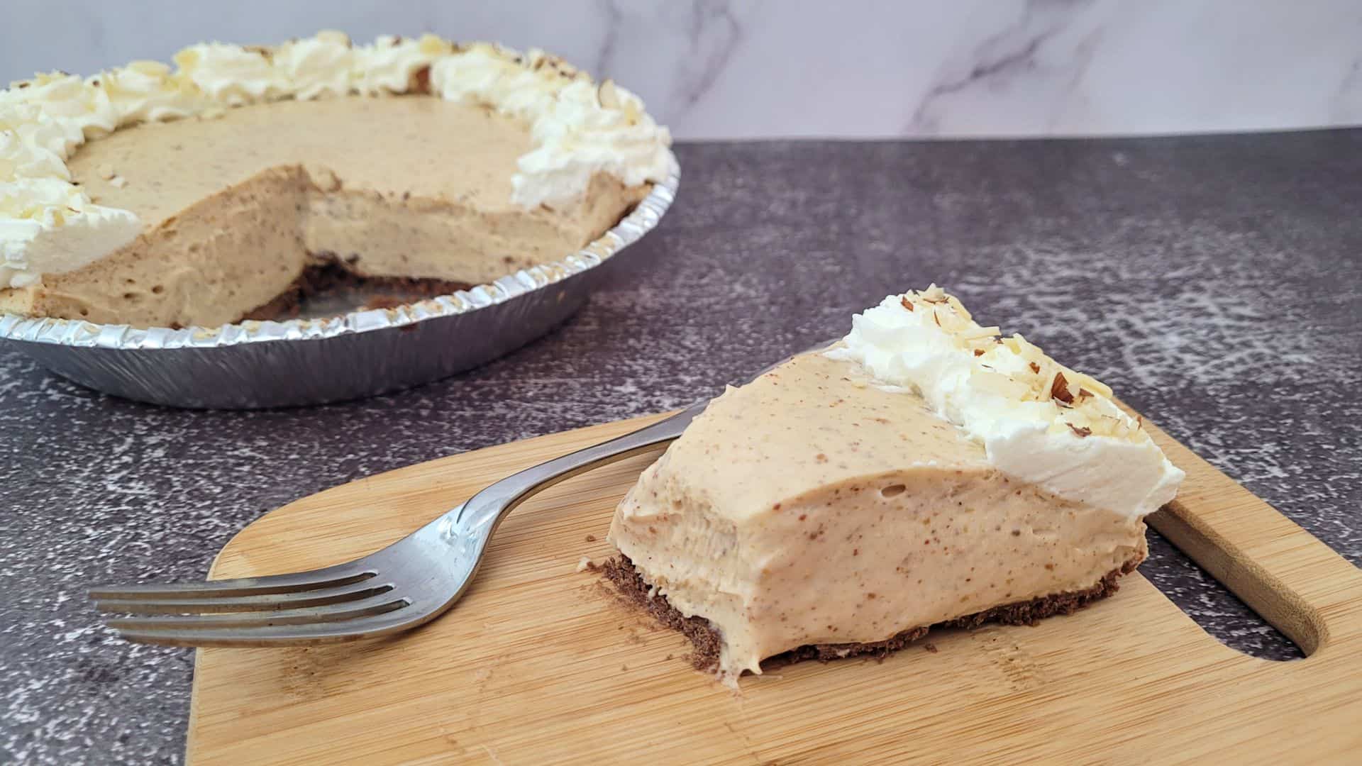 slice of almond butter pie on a wooden board with remainder of pie in background