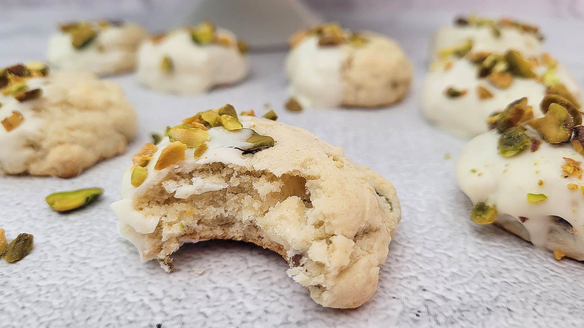 pistachio white chocolate cookies on a countertop with one cookie bitten into