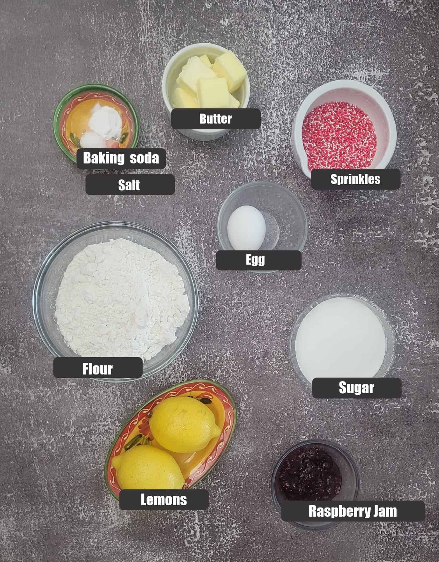 ingredients needed to make cookies including sprinkles, raspberry jam, granulated sugar, flour, egg, butter, baking soda, salt and lemons