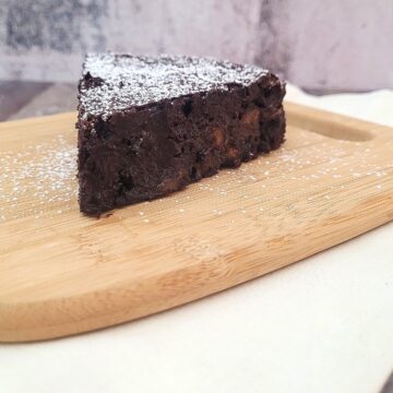 image of flourless chocolate banana cake sprinkled with powdered sugar on a wooden platter