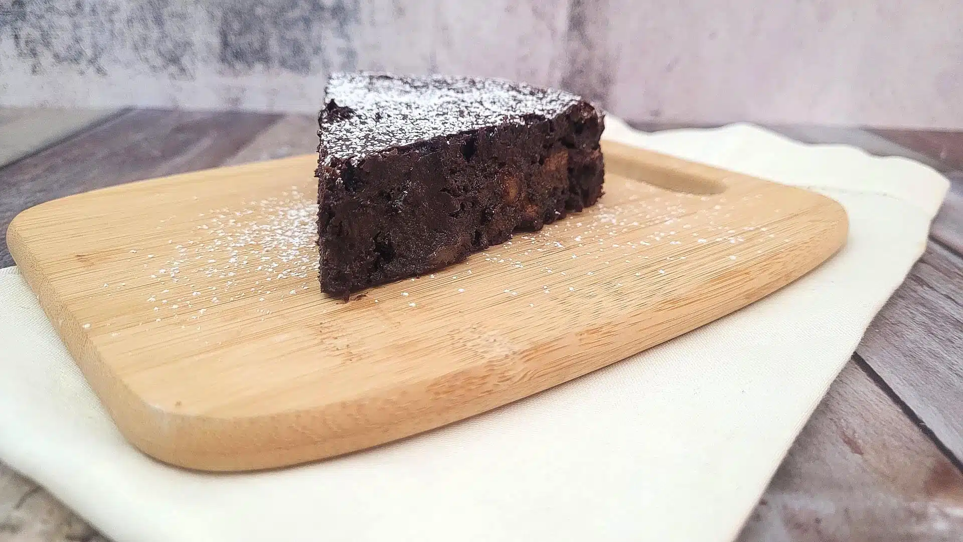 image of flourless chocolate banana cake sprinkled with powdered sugar on a wooden platter