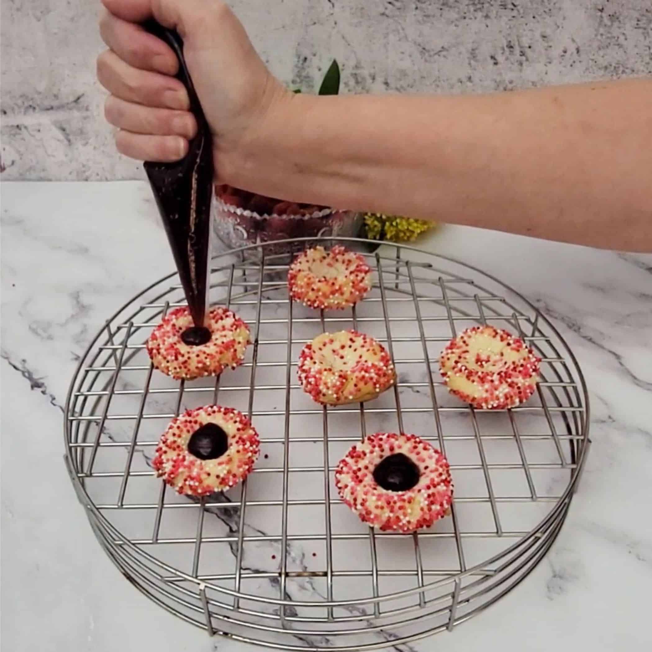 using a pastry bag to add raspberry jam to lemon thumbprint cookies