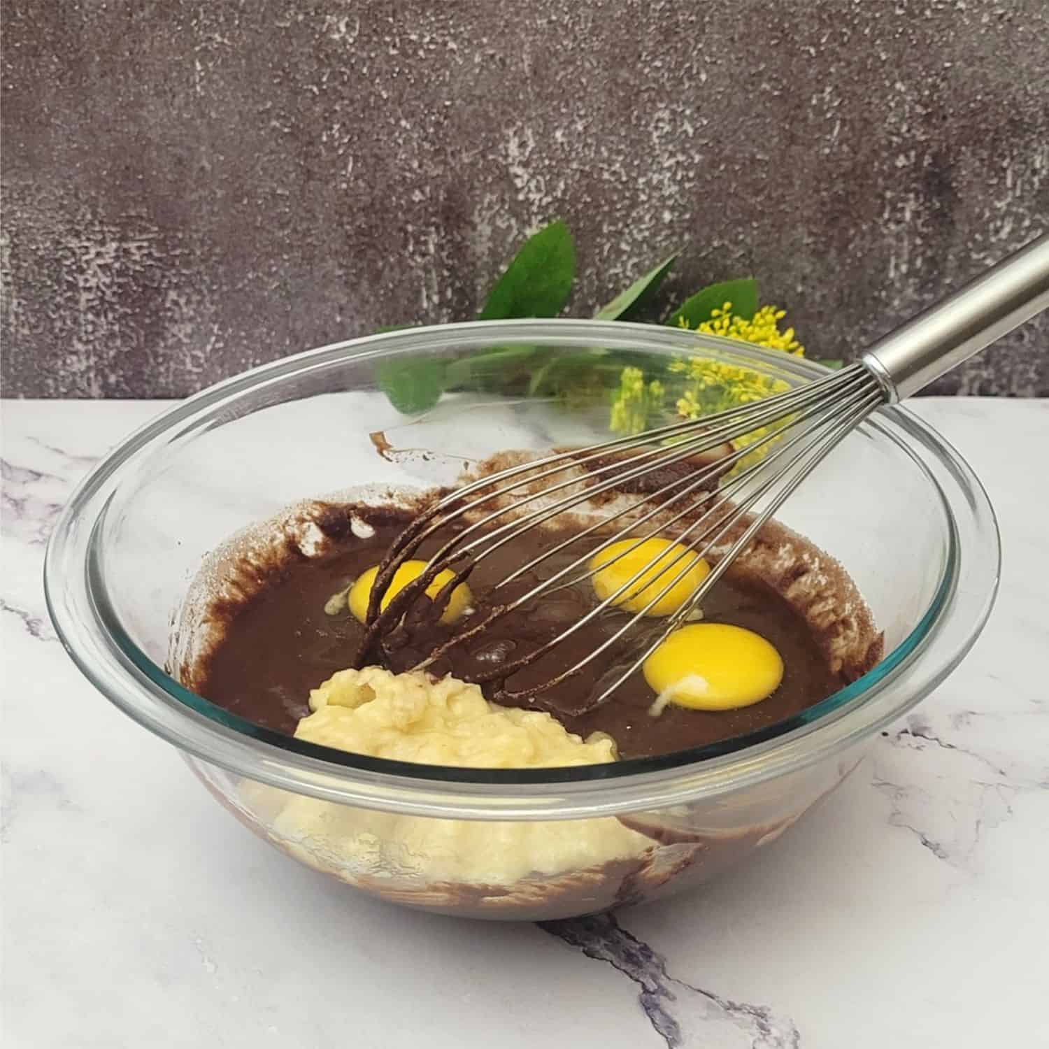 eggs and mashed bananas added to mixing bowl to make cake batter using a hand whisk