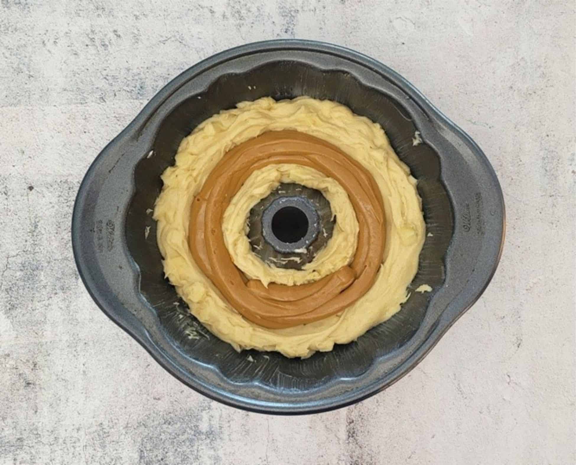 Bundt pan with half of the cake batter added and caramel piped into the center