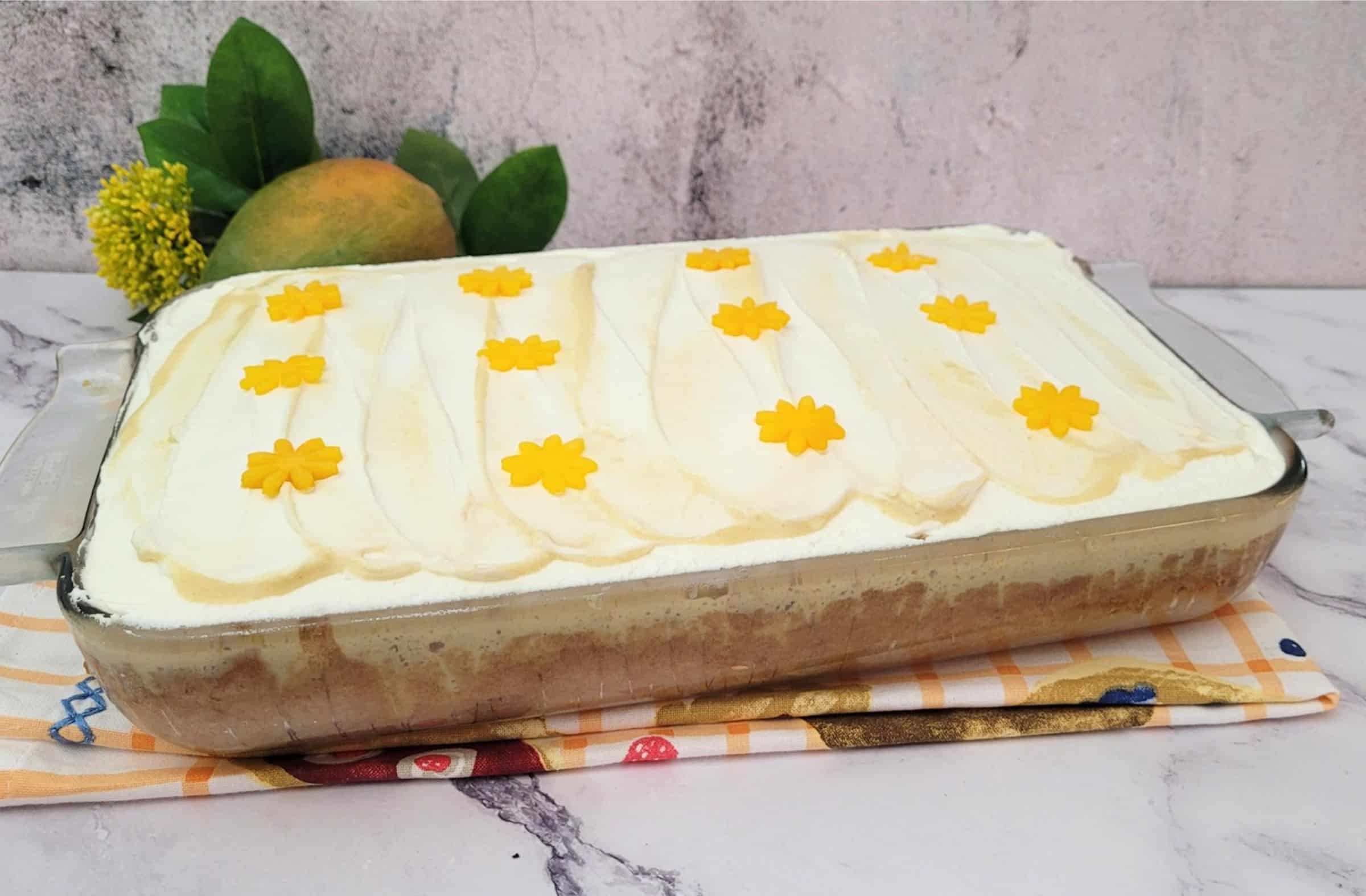 pan of finished mango tres leches cake with whipped cream and mango flower cutouts on top