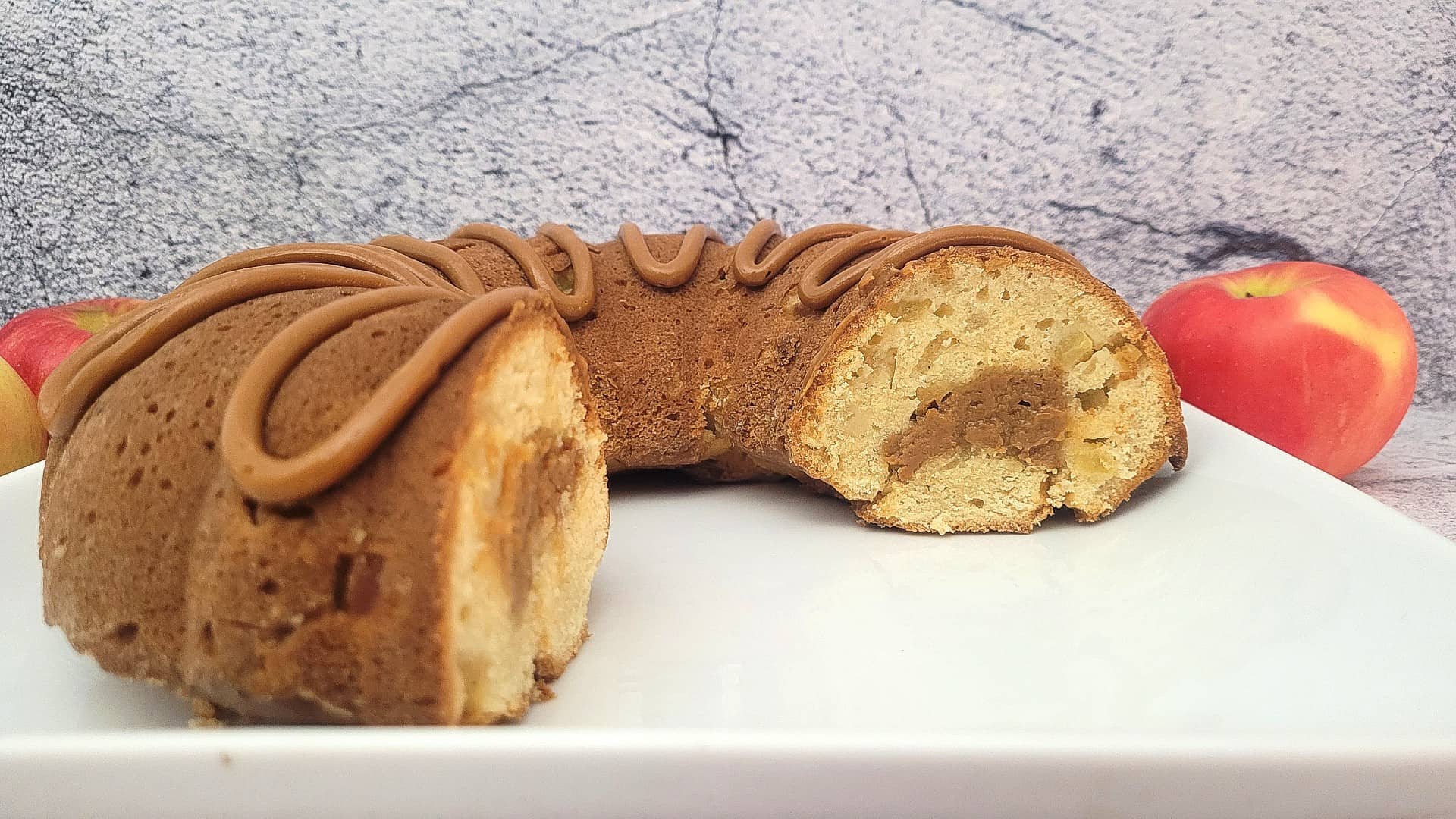 Bundt cake on a serving platter with several slices missing and apples in the background