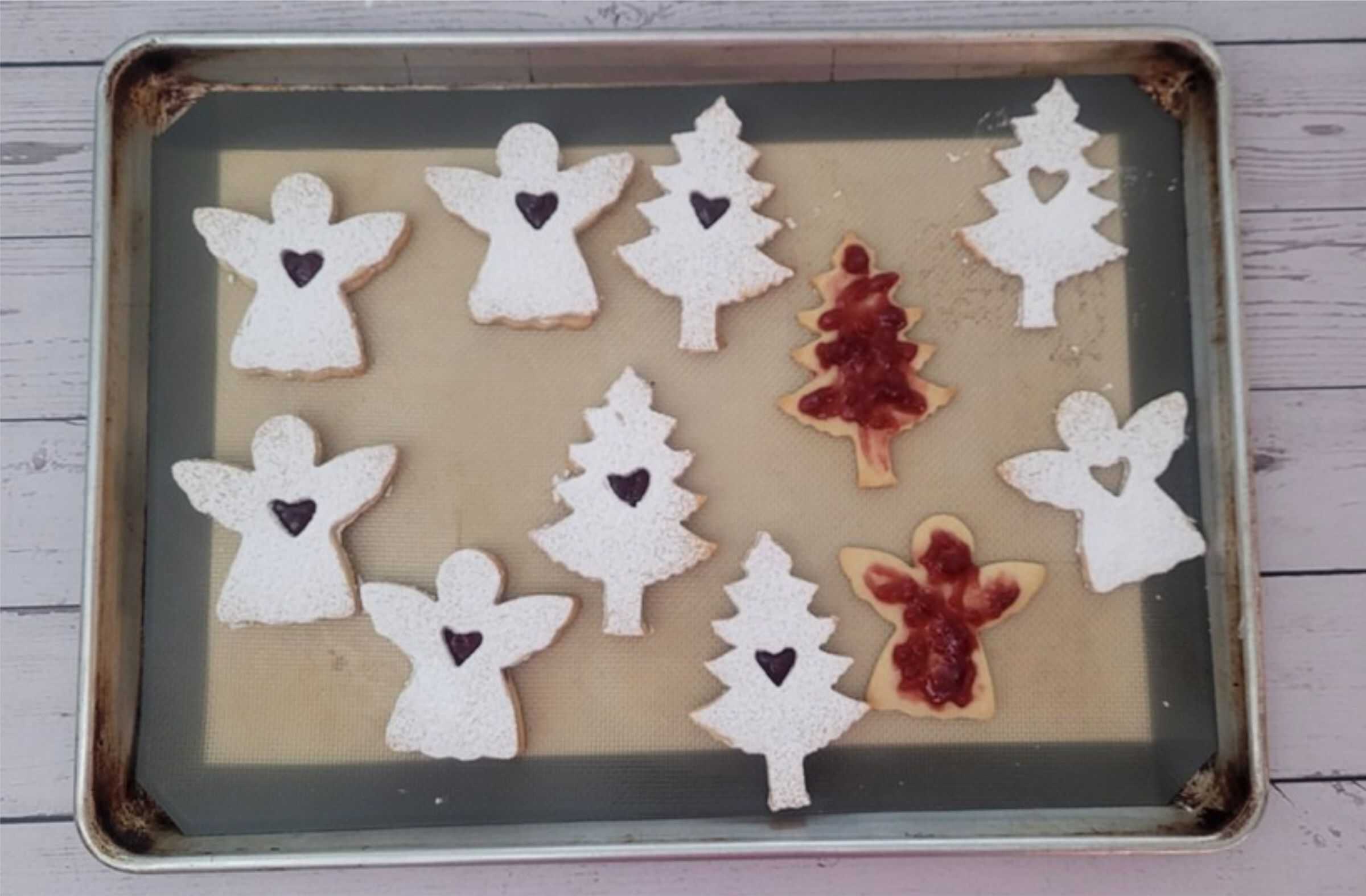 Linzer cookies in Christmas and angel shapes being assembled on a sheet pan