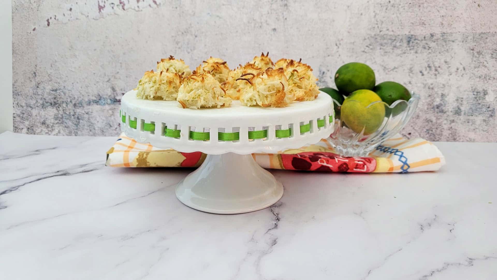 lime coconut macaroons on a small cake stand and whole limes in a bowl