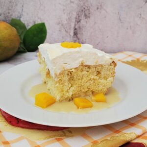 slice of mango tres leches on a cake with extra mango pieces