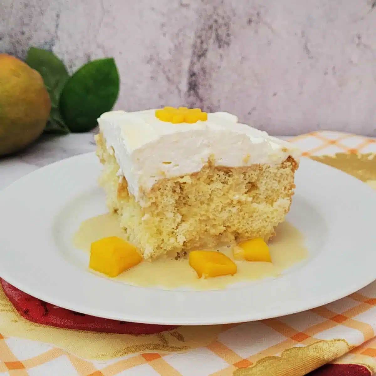 slice of mango tres leches on a cake with extra mango pieces