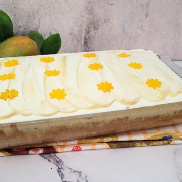 9 inch by 13 inch pan with finished mango Tres Leches cake on a marble countertop