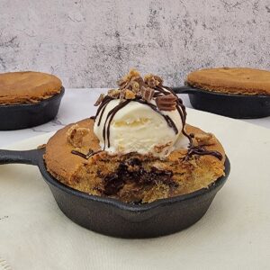 close up of inside of skillet cookie with peanut butter cups and chocolate ganache and a scoop of ice cream on top