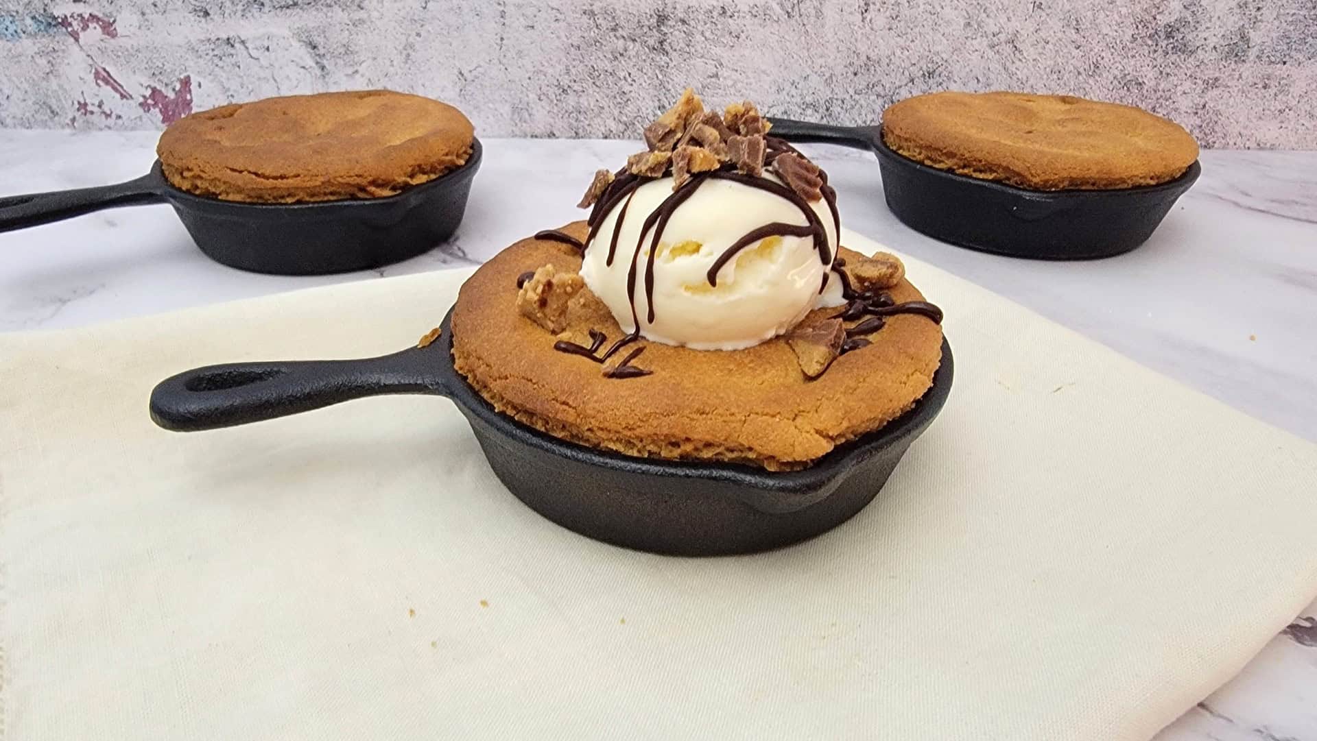 cookies in skillet pans filled with Reese's cups and topped with vanilla ice cream