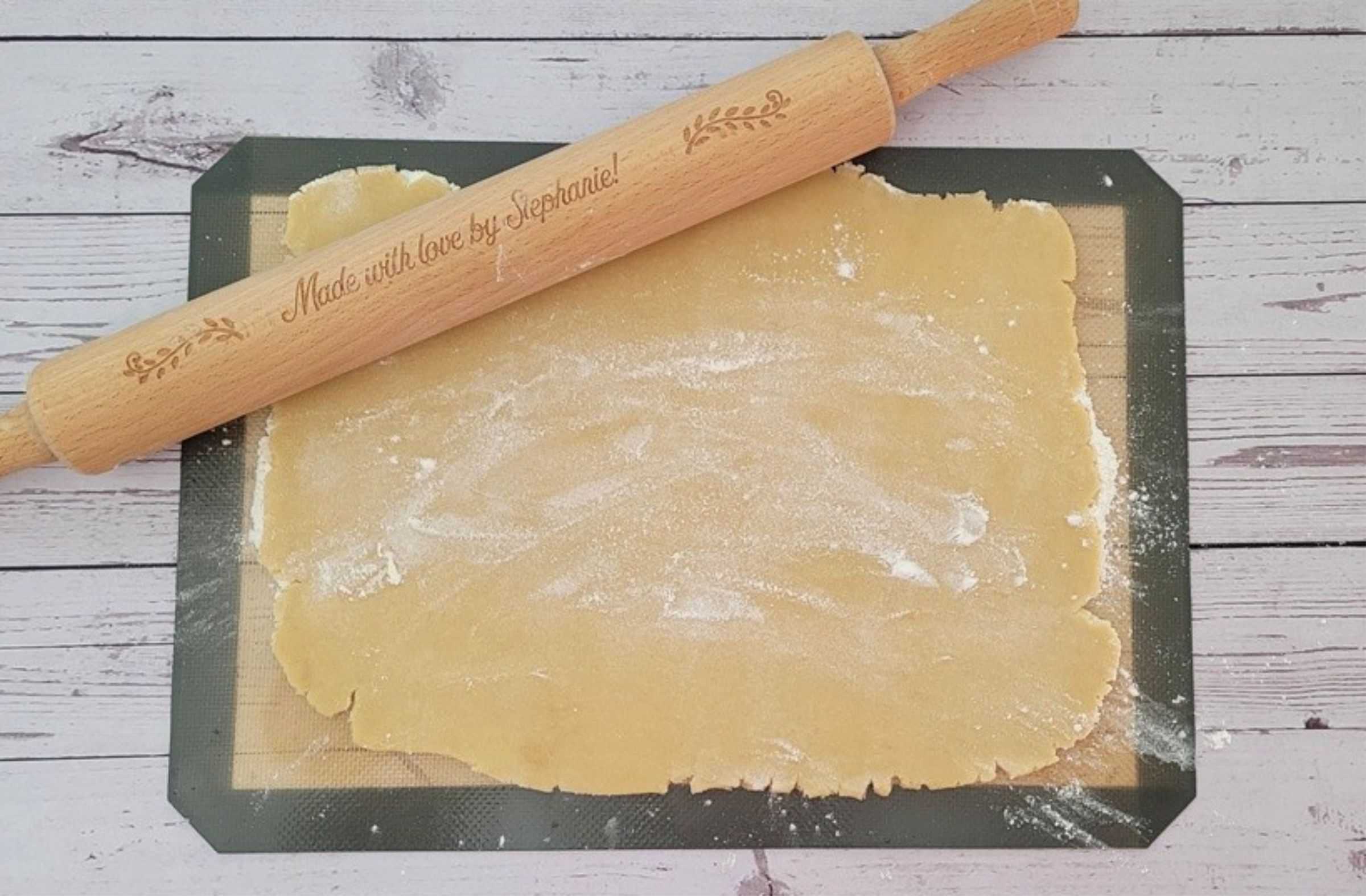 cookie dough rolled out on a silicone baking mat and a rolling pin in picture