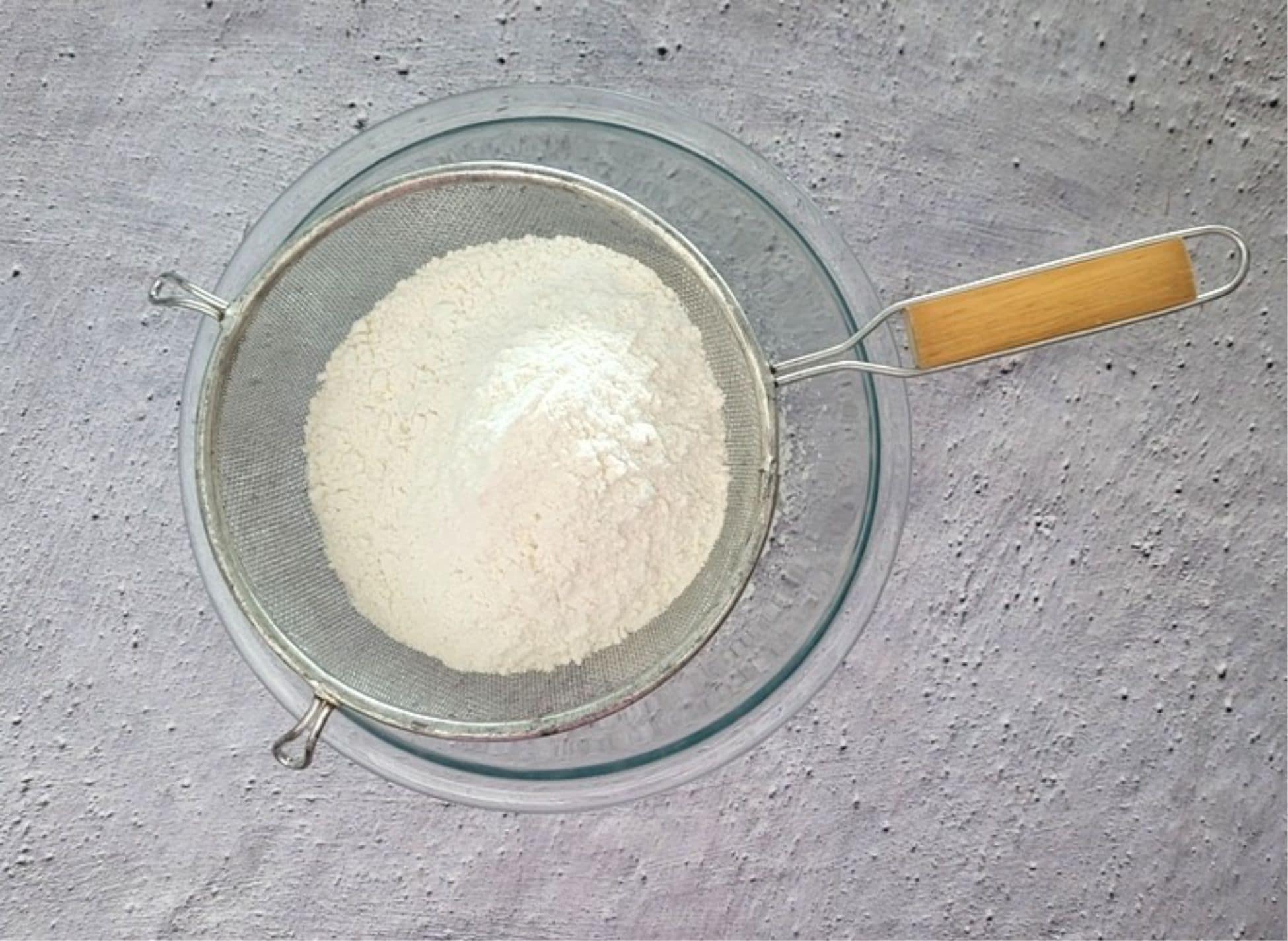 flour, baking soda and salt in a sieve being sifted to remove lumps
