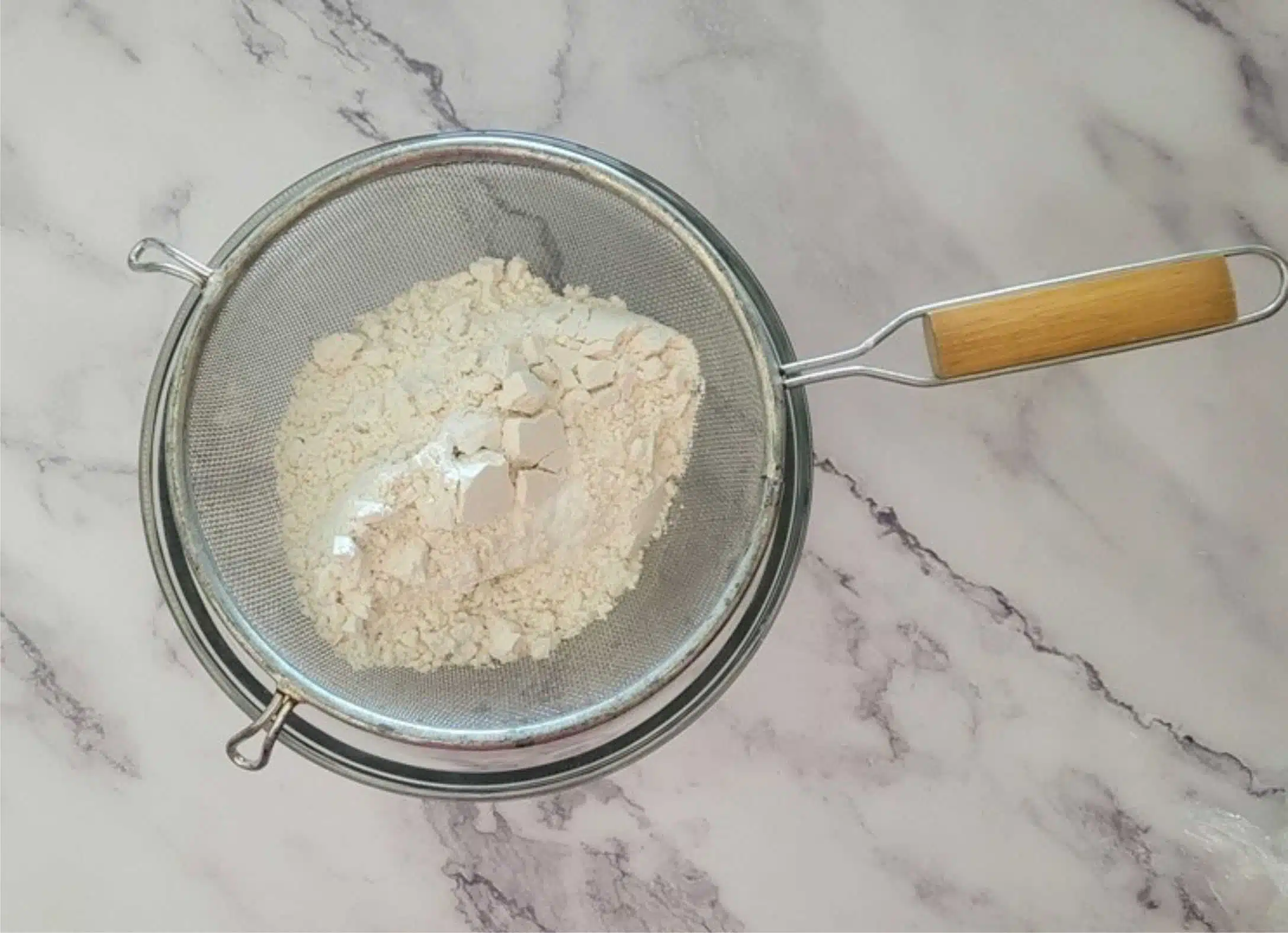 a mesh sieve with flour, baking soda and salt being sifted together