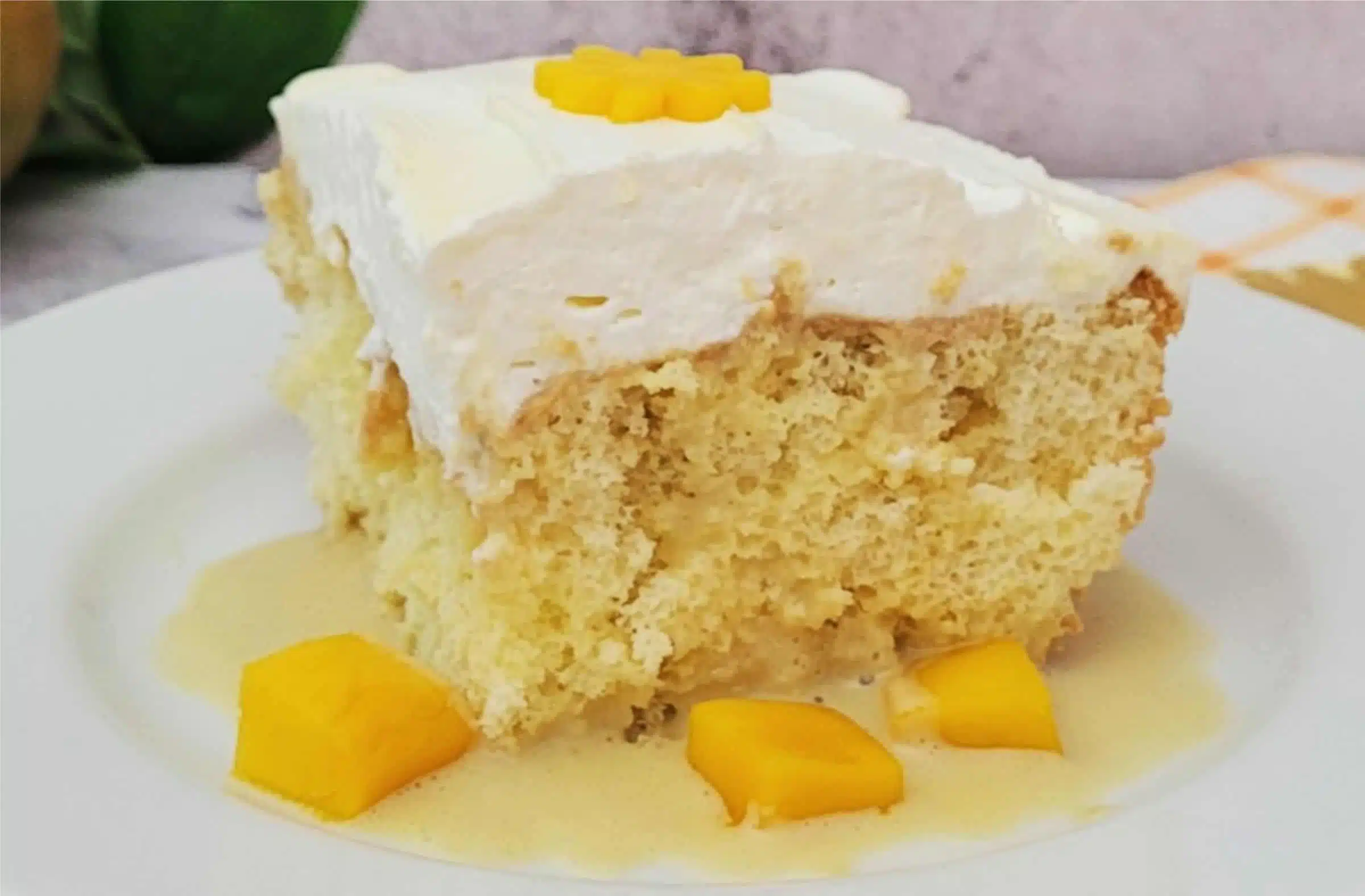 large slice of mango Tres Leches cake on a white plate with extra pieces of mango for taste and color