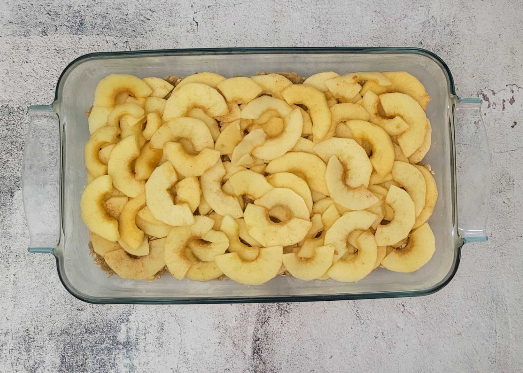 apple slices layered in a baking pan over the bottom layer of oatmeal cookie dough