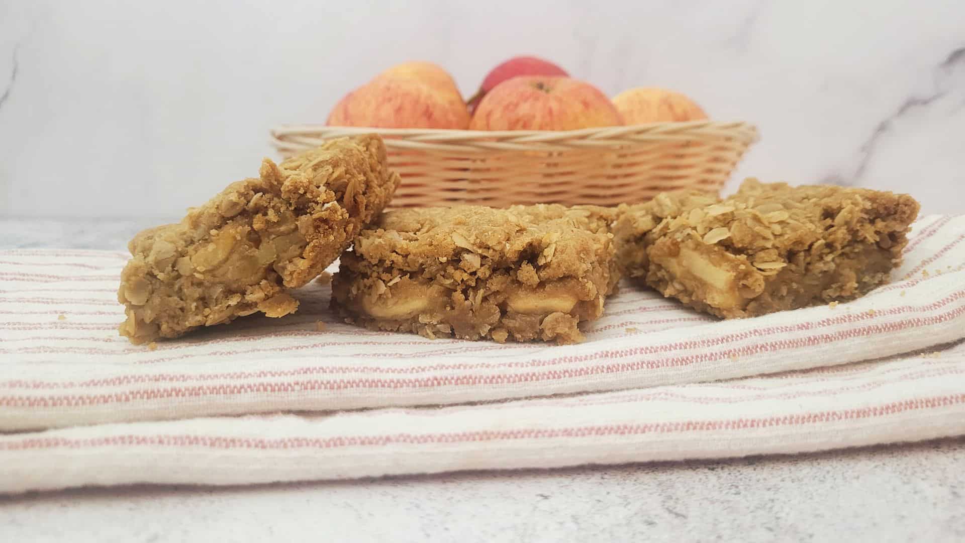 three oatmeal apple cookie bars on a napkin with apples in the background