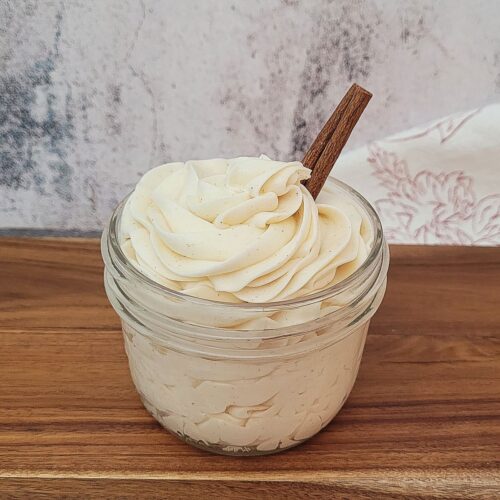 mason jar filled with cinnamon cream cheese icing and a cinnamon stick placed in the jar