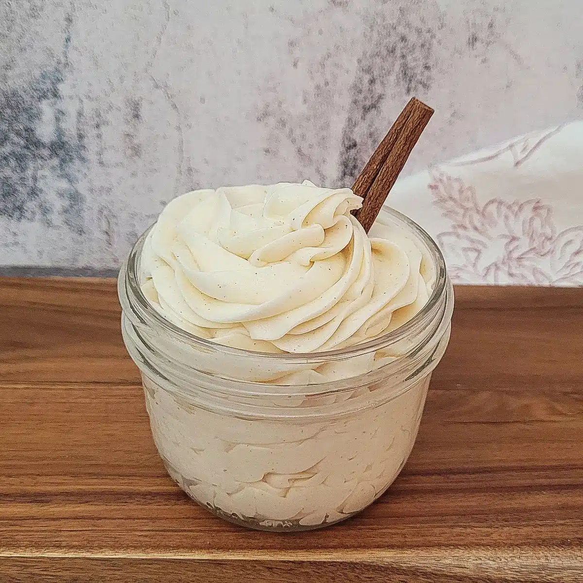 mason jar filled with cinnamon cream cheese icing and a cinnamon stick placed in the jar