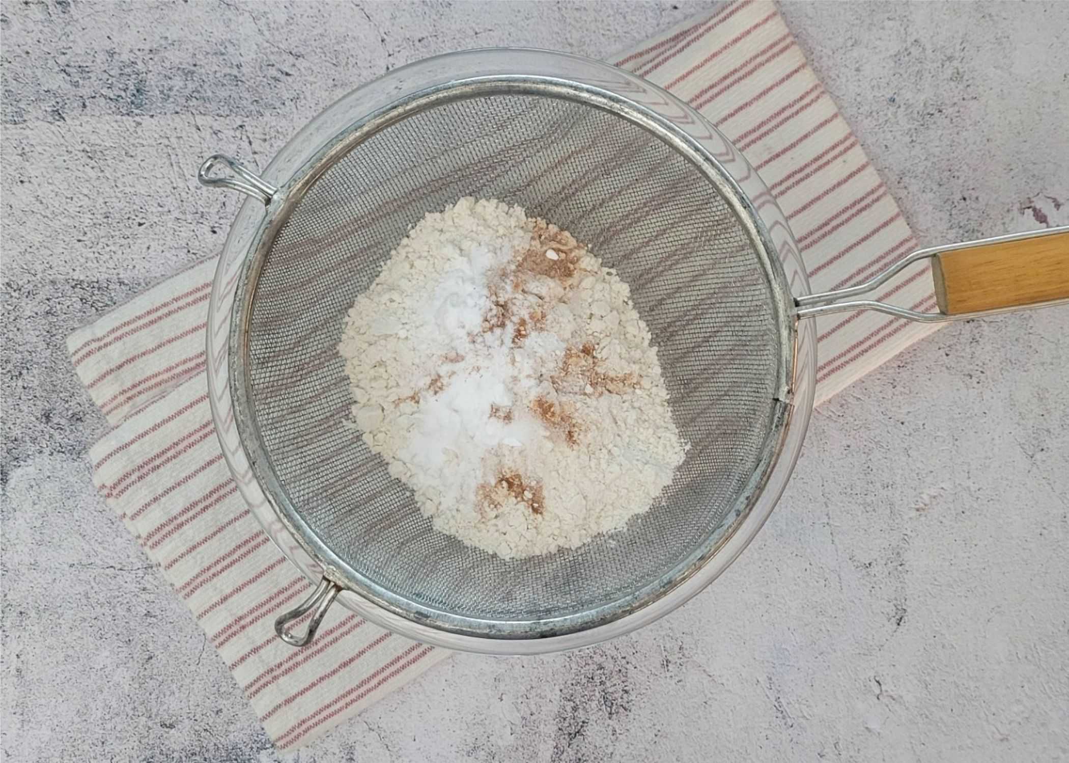 dry ingredients being sifted together for cookie dough, including flour, baking soda, salt and ground cinnamon